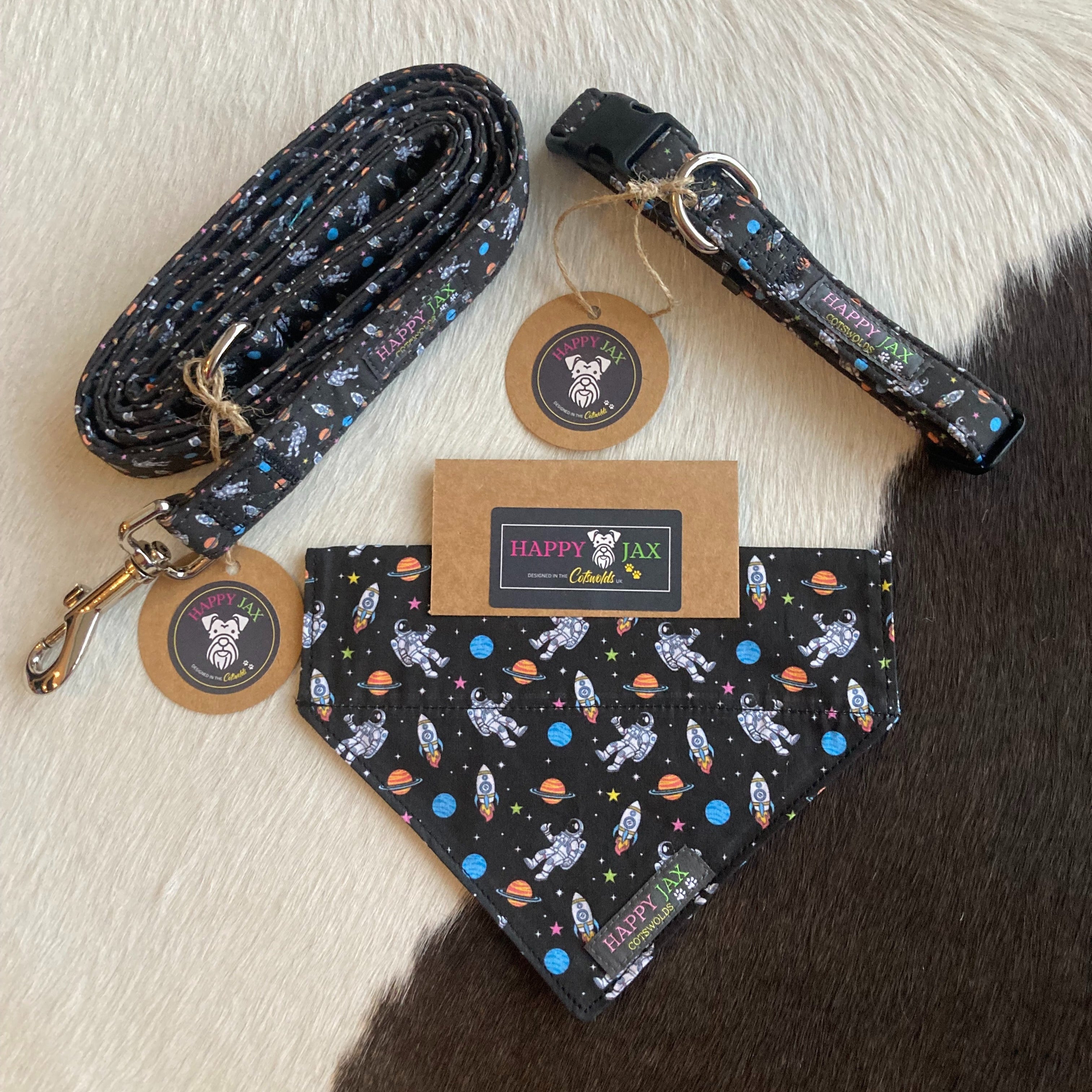 Bundle with an animal collar, bandana and lead in a bright and colourful design of astronauts and rocket ships surrounded by planets and stars on a black background. Products are suitable for both cats and dogs and available in a range of sizes made with cotton and designed in the Cotswolds.