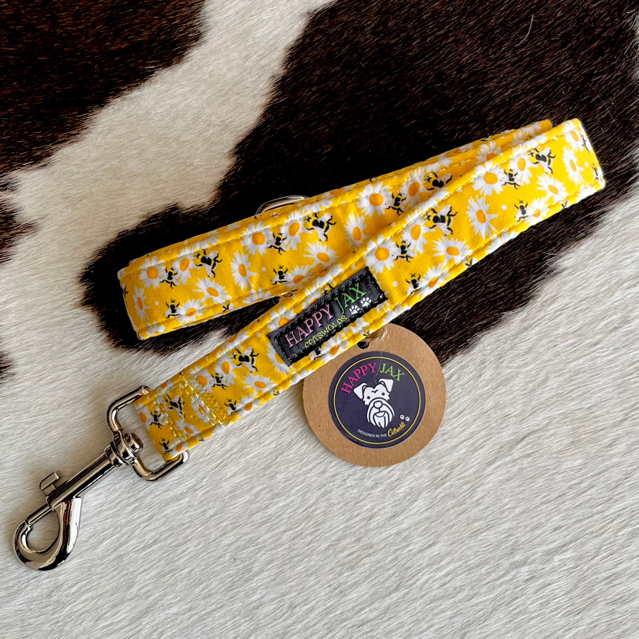 Yellow floral dog leash with bees and a branded tag on a textured surface