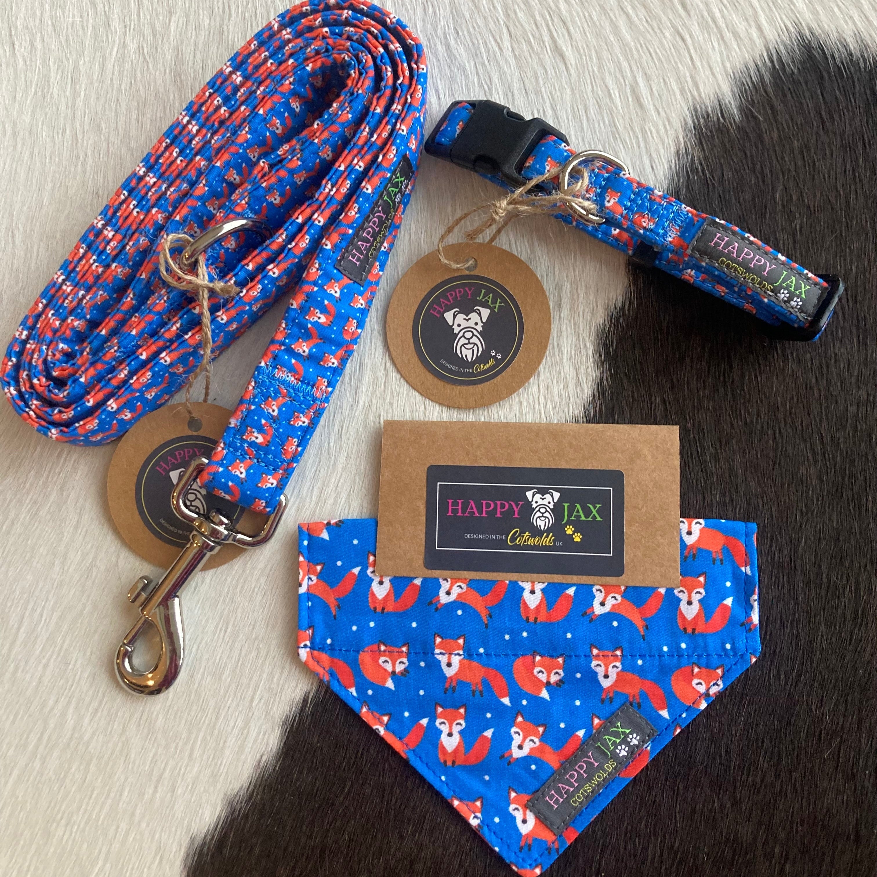 Bundle with an animal collar, bandana and lead in a bright and colourful design of orange foxes blowing on a navy blue background. Products are suitable for both cats and dogs and available in a range of sizes made with cotton and designed in the Cotswolds.